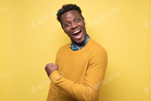 Preview: Smiling african man with the fists up on yellow wall. Studio shot