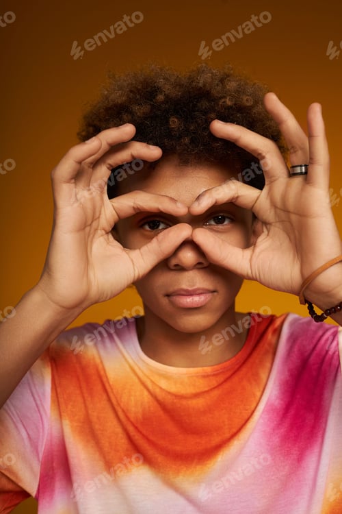 Preview: Close-up of teenage boy keeping hands by his eyes during photo shooting