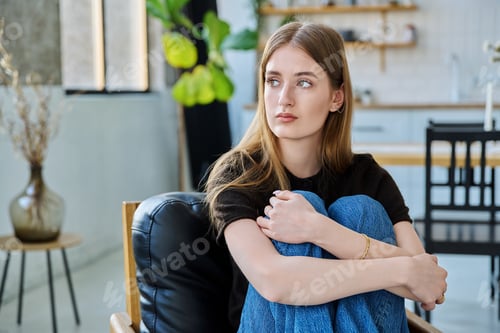 Preview: Sad unhappy thoughtful young woman sitting in armchair at home