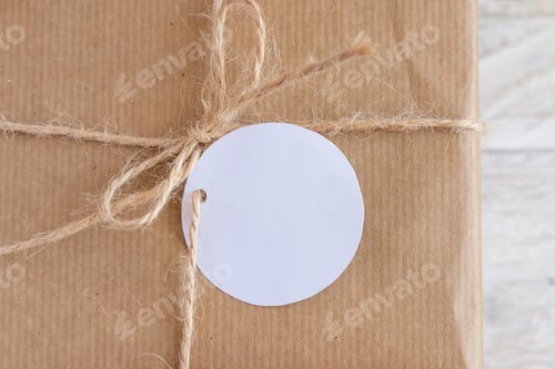 Preview: Kraft paper wrapped present with round blank gift tag top view, Mockup