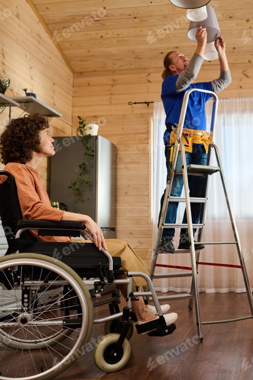 Preview: Mature electrician standing on stepladder and changing bulbs in chandelier