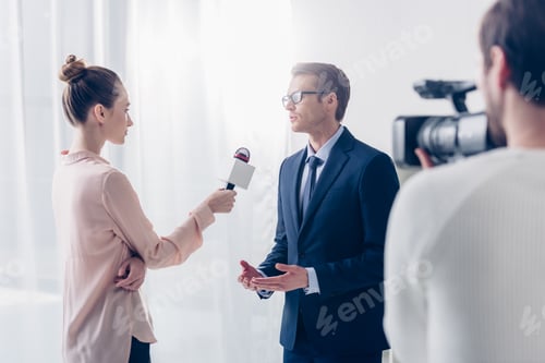 Preview: handsome businessman in glasses giving video interview to beautiful journalist in office