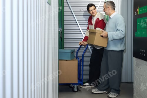 Preview: Middle Aged Man and Teenager Carrying Boxes in Storage Facility