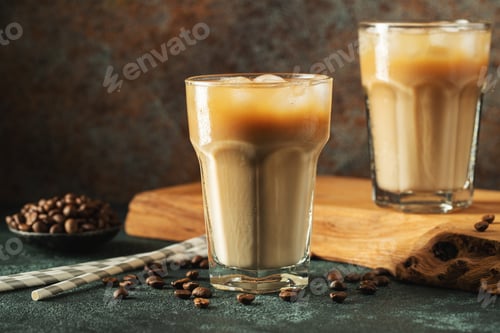 Preview: Ice coffee in a tall glass with cream poured over, ice cubes and beans on a dark concrete table.