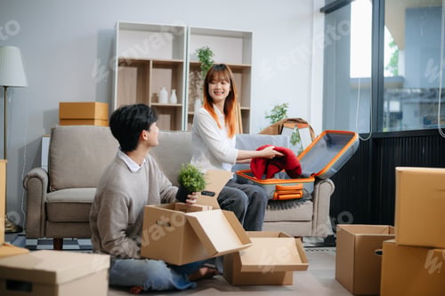 Preview: Young couple preparing for a move, packing boxes and a suitcase in a cozy living room. Perfect for