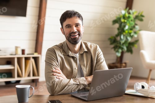 Preview: Cheerful man sits at wooden table in well-lit home office