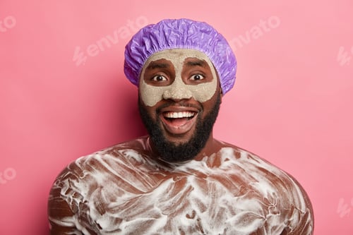 Preview: Positive naked gentleman wears facial mask, has foam on body, enjoys taking shower and relaxation af