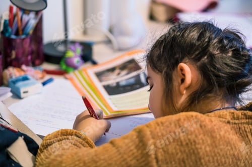 Preview: Young girl doing homework and writing on paper at home