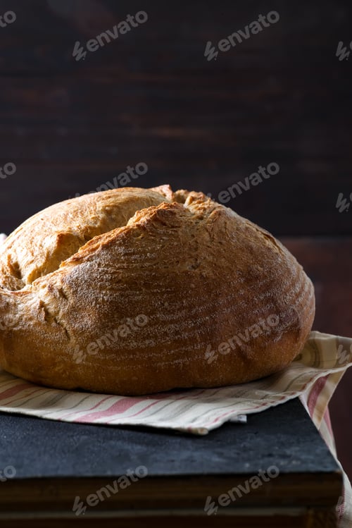 Preview: Round freshly baked rustic rye round bread with wheat ears and napkin on a dark background, copy
