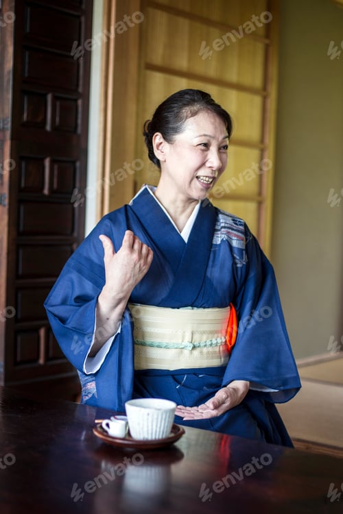 Preview: Smiling Japanese woman wearing blue kimono sitting on floor in traditional Japanese house.