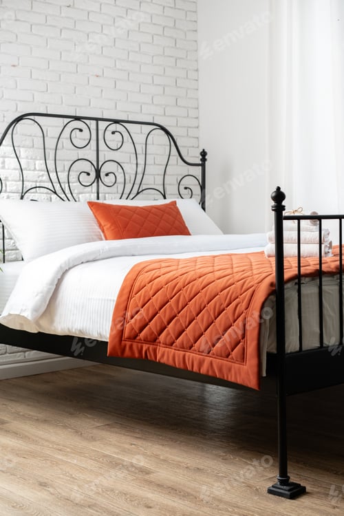 Preview: Modern Bed With Ornate Iron Headboard and Orange Throw Blanket in a Light and Airy Bedroom