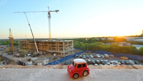 Preview: small red toy car against the backdrop of a house under construction and sunset
