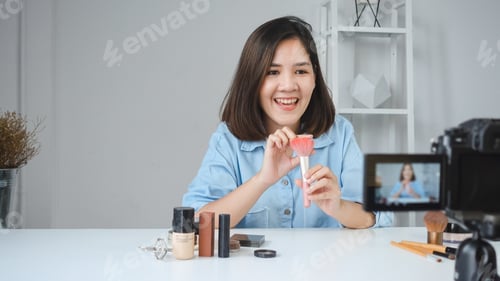 Preview: Happy smiling asian woman or beauty blogger with brush and camera recording video.