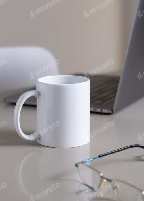 Preview: White coffee mug on grey office table against laptop, glasses and pencil closeup, mockup