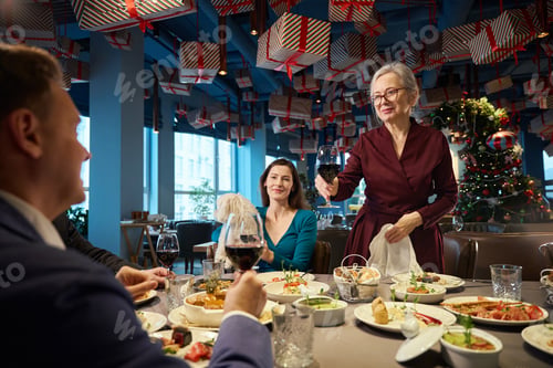 Preview: Old woman raising glass of wine toasting congratulating with New Year holidays