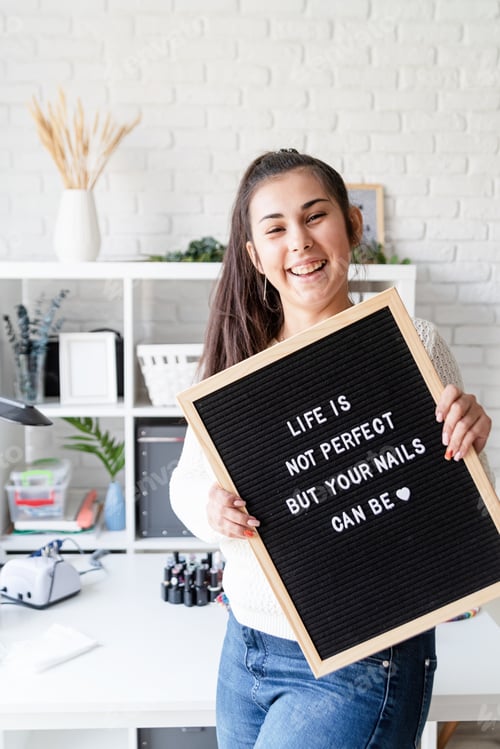 Preview: Manicure master in nail salon holding black felt letter board with text Life Is Not Perfect, But You