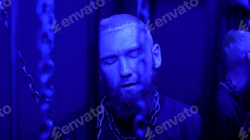 Preview: A young stylish man at the event standing with chains around his neck that hanging from the ceiling