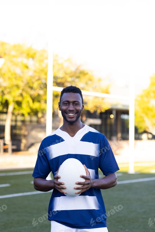Preview: African American young male athlete holding a rugby ball, standing on field outdoors, copy space