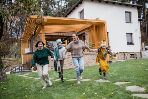 Preview: Two happy sisters with mother and grandmother holding hands and running outdoors in garden in autumn