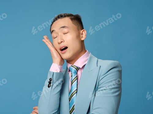 Preview: Asian man touching his face with his hand on a blue background