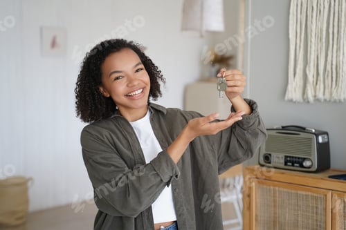 Preview: Home ownership. Young african american girl is holding and showing key from new home.
