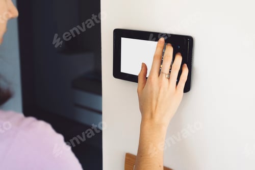 Preview: Young unrecognizable caucasian woman answering the door bell on modern home security device with a s