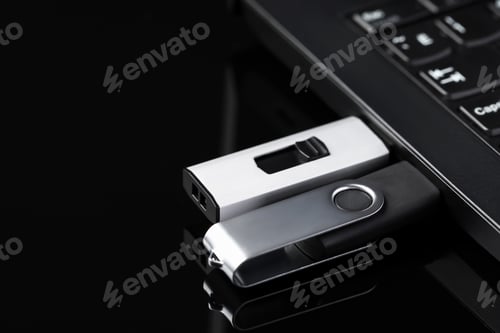 Preview: Modern usb flash drives attached into laptop on black table, closeup. Space for text
