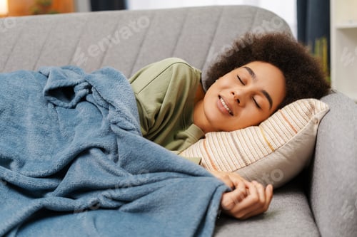 Preview: Cute African American woman with curly hair lying on pillow covered with blanket on comfortable sofa