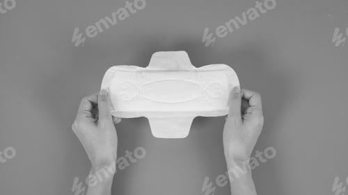 Preview: Hands hold a sanitary napkin with wings top angle view. Black and white picture.