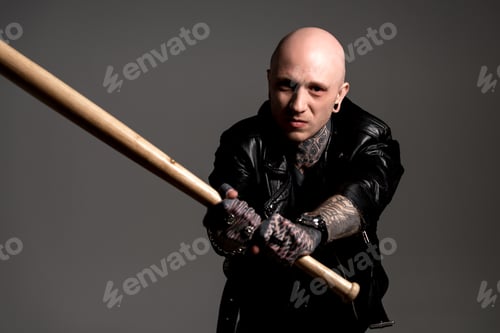 Preview: aggressive tattooed man in leather jacket holding baseball bat and looking at camera isolated on