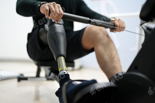 Preview: disabled athlete man, with leg prosthesis working out on sport machine