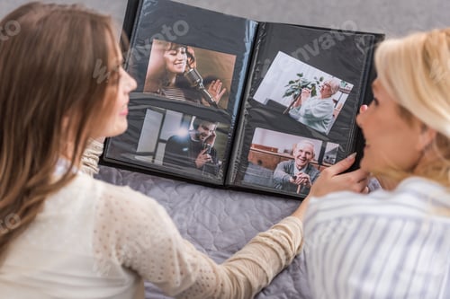 Preview: overhead view of mother and daughter talking while lying on bed and looking at photo album