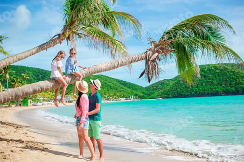 Preview: Little girls having fun sitting on the palm tree. Happy family relaxing on tropical beach with white