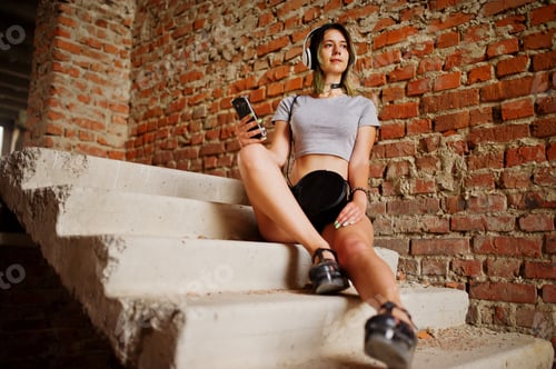Preview: Girl wear on shorts with big headphones at abadoned factoty with brick walls.