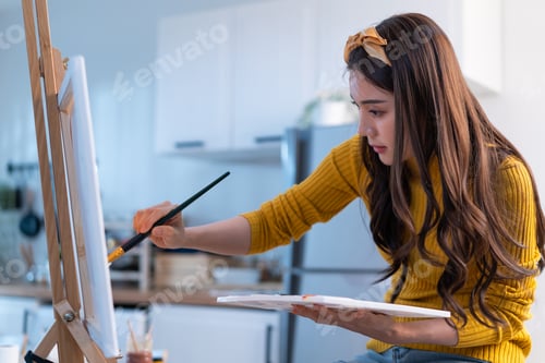 Preview: Asian young talented woman artist coloring on painting board in house.