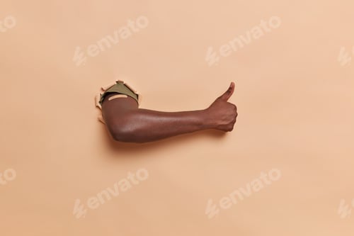 Preview: Unrecognizable dark skinned man breaks through paper background shows black arm with adhesive plaste