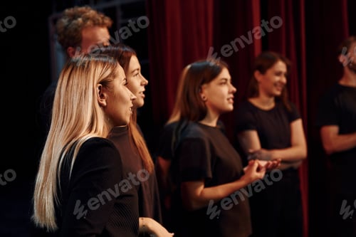 Preview: Side view. Group of actors in dark colored clothes on rehearsal in the theater