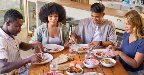 Preview: Group Of Multi-Racial Friends Sitting Around Table Enjoying Meal At Home Together