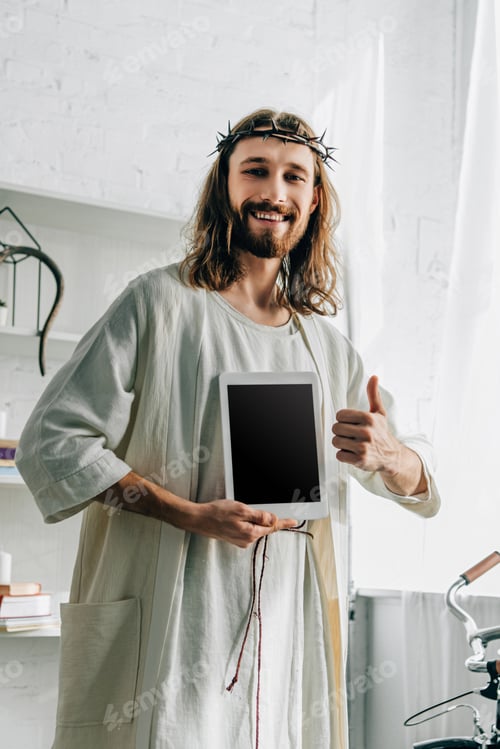 Preview: happy Jesus in crown of thorns doing thumb gesture and showing digital tablet with blank screen at