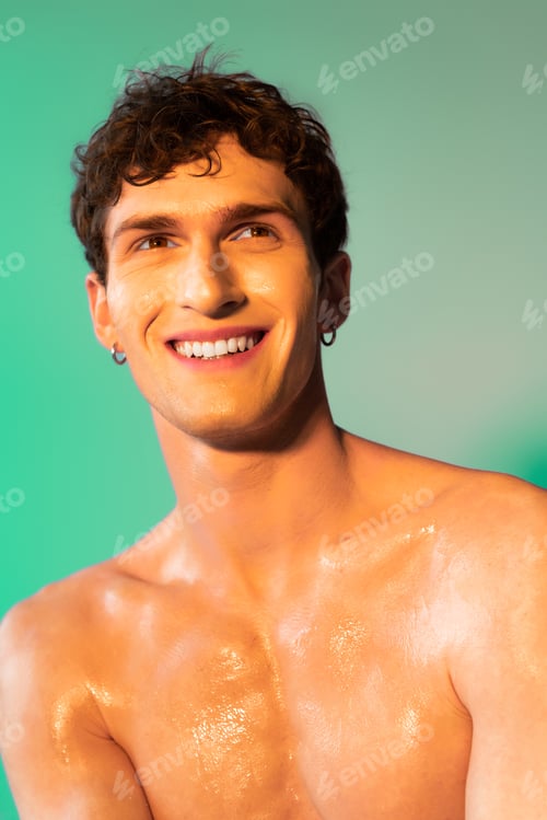Preview: Portrait of smiling shirtless man with oil on skin on green background