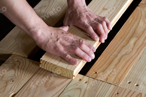 Preview: Close up of strong muscular hands of professional carpenter installing natural wooden new planks on