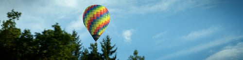 Preview: 4x1 banner with flying multi-color balloon against blue sky with clouds and of a green forest