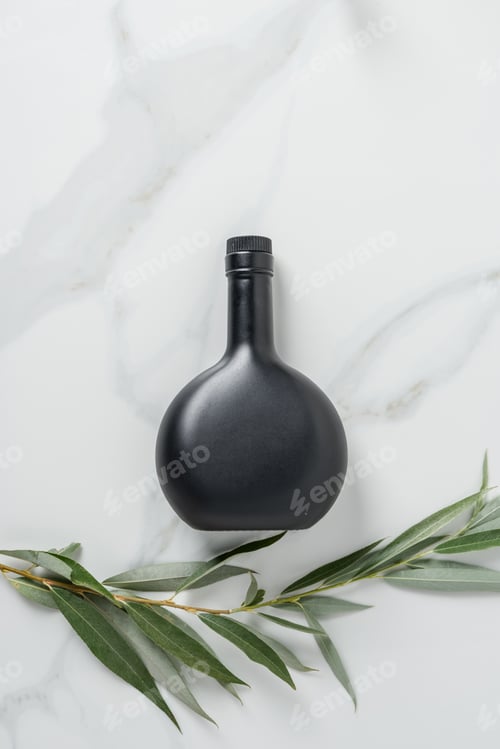 Preview: top view of black bottle of olive oil and twig on marble table