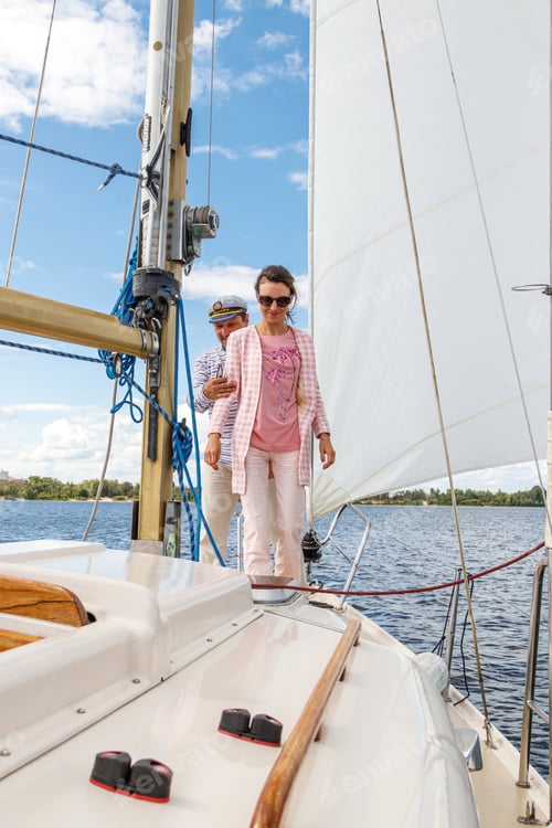 Preview: sailor man in a cap with a girl on a boat under sail against the sky and water