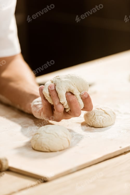 Preview: cropped shot of baker kneading dough for pastry on messy table