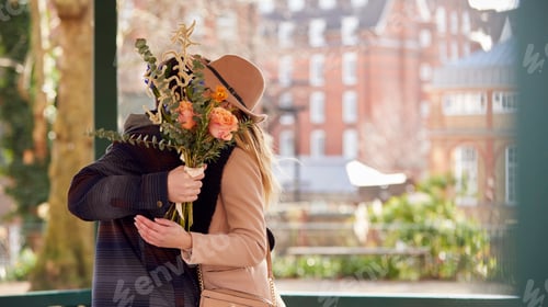 Preview: Romantic Man Hugging Young Woman With Faces Hidden Behind A Bouquet Of Flowers He Gives Her
