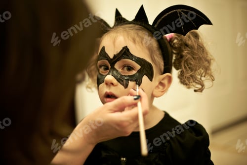 Preview: Mother painting daughters face for halloween bat costume