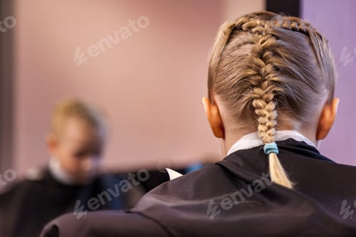 Preview: Hair salon, little girl with fashionable braids hairstyle sitting at mirror in modern barbershop
