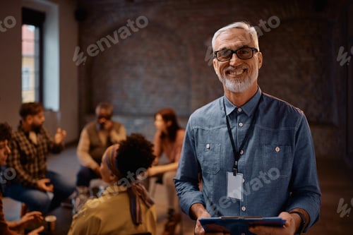 Preview: Happy mature psychotherapist during group meeting at mental health center looking at camera.