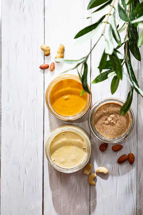 Preview: Jars of Almond, Cashew and Peanut Butter on a White Wooden Table.